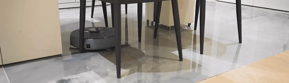 Coverage along furniture tests well; here the robot threads between dining chair legs near a wall.