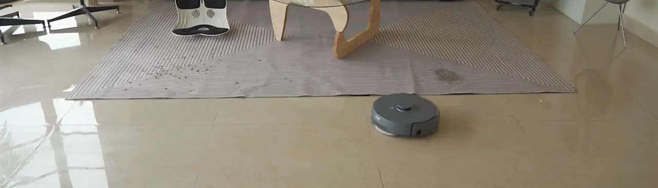 Everyday debris clears as the robot passes; here a scatter of dark grit waits on the tile ahead.